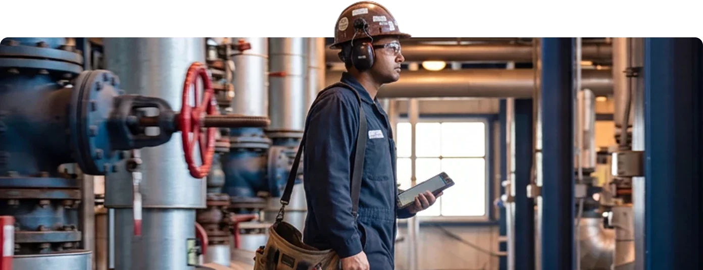 A maintenance technician walking through a plant with a tablet and tool bag